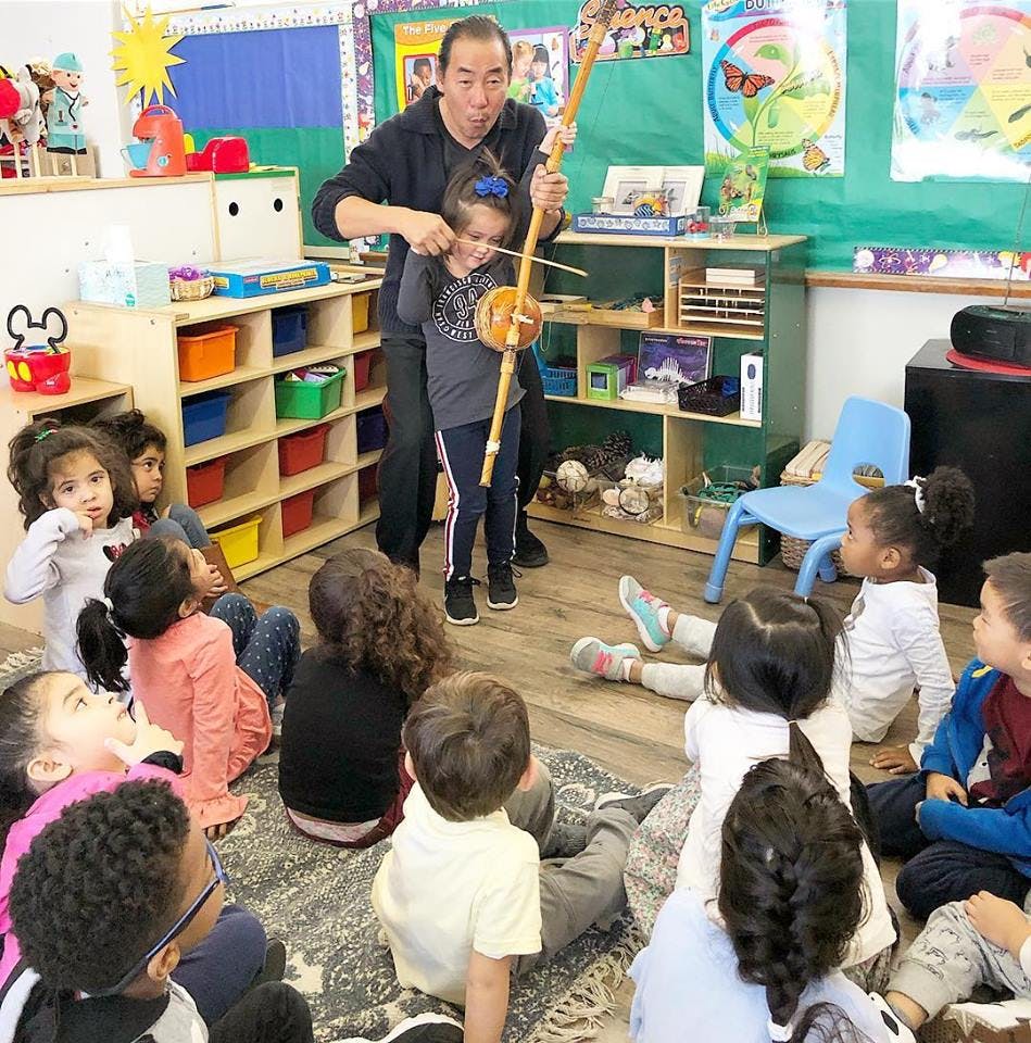 Adult helping a child play a stringed instrument for other children