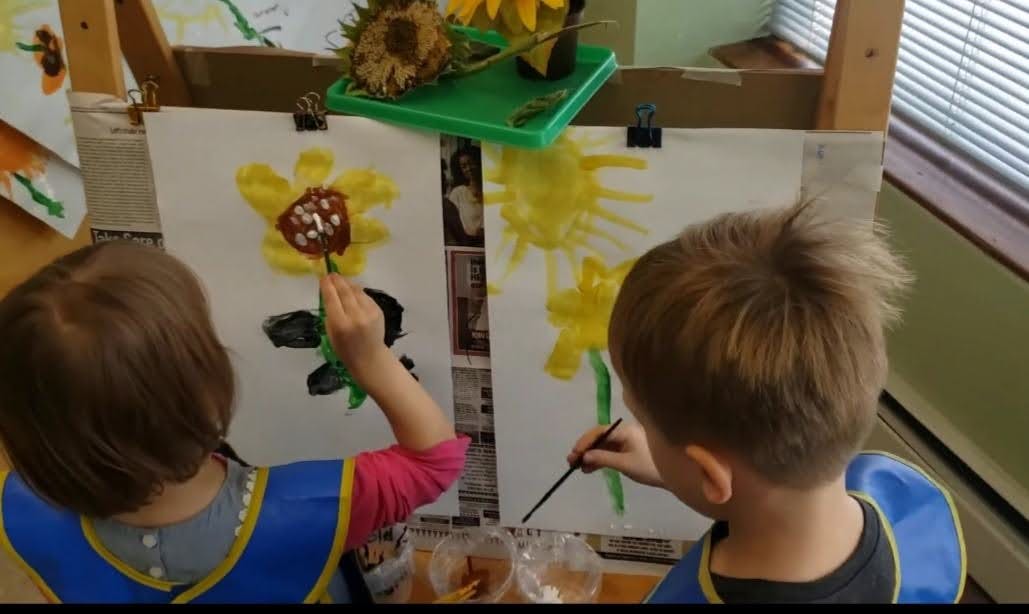 Two children painting sunflowers in a classroom