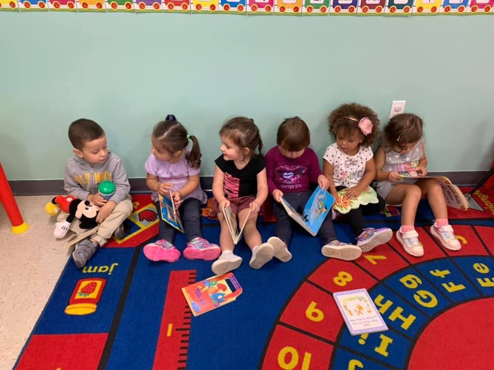 Six children sitting on a rug reading books in a classroom