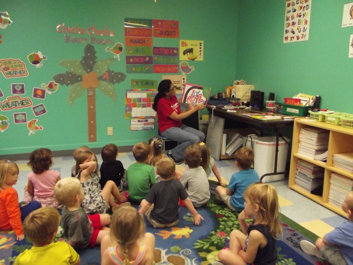 Person reading a book to a group of children in a classroom