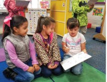 Three children sitting on the floor looking at a paper