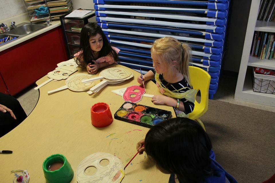 Children painting paper masks at a table