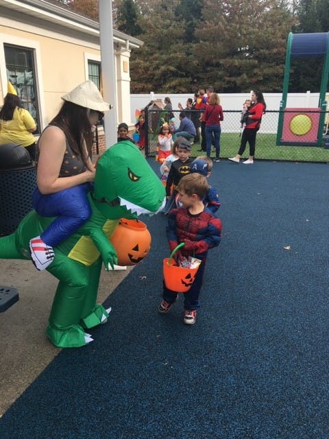 Person in dinosaur costume with child in Spiderman costume holding pumpkin bucket