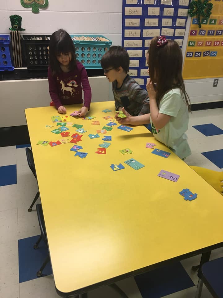Three children playing with colorful puzzle pieces on a yellow table