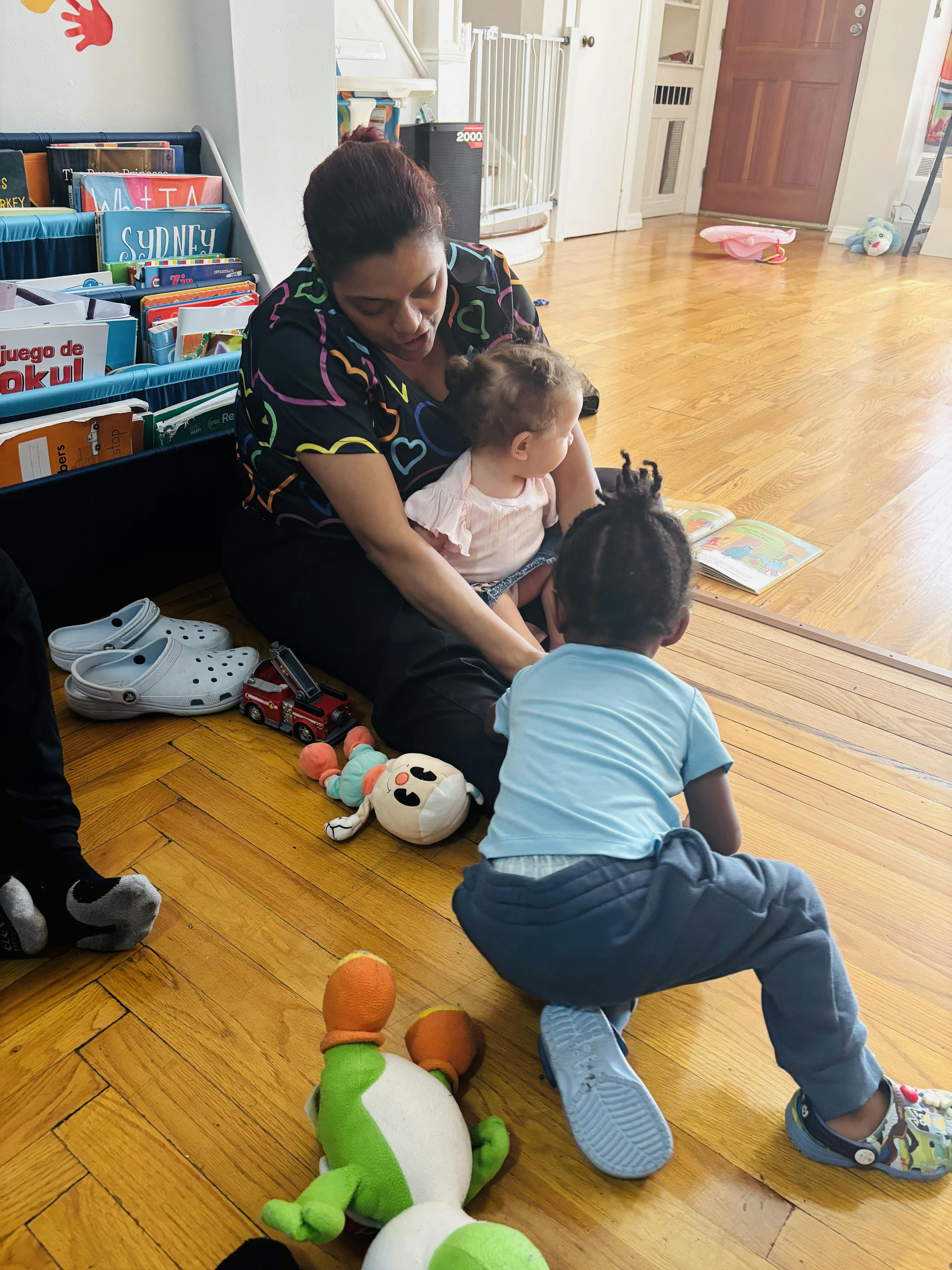 Adult sitting on the floor reading a book to two children