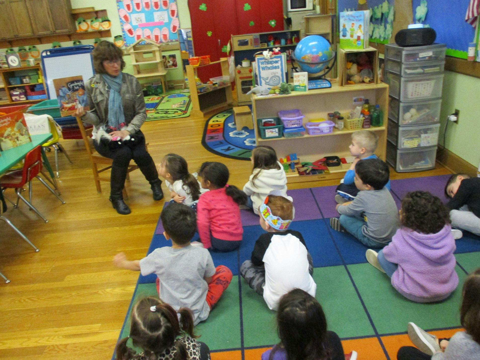 Adult sitting in a chair reading to children sitting on a rug