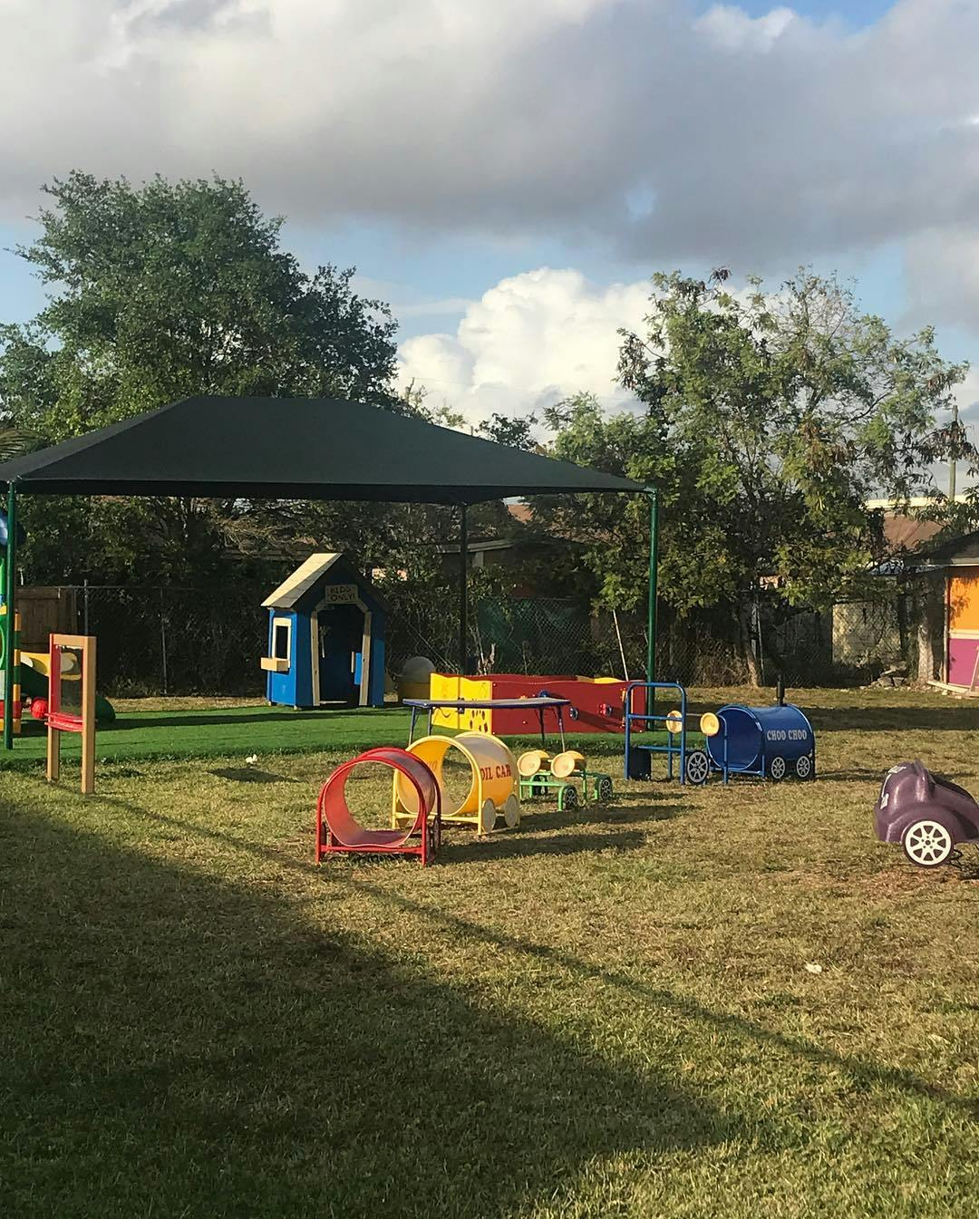 Outdoor play area with a shade structure, playhouse, and colorful play equipment