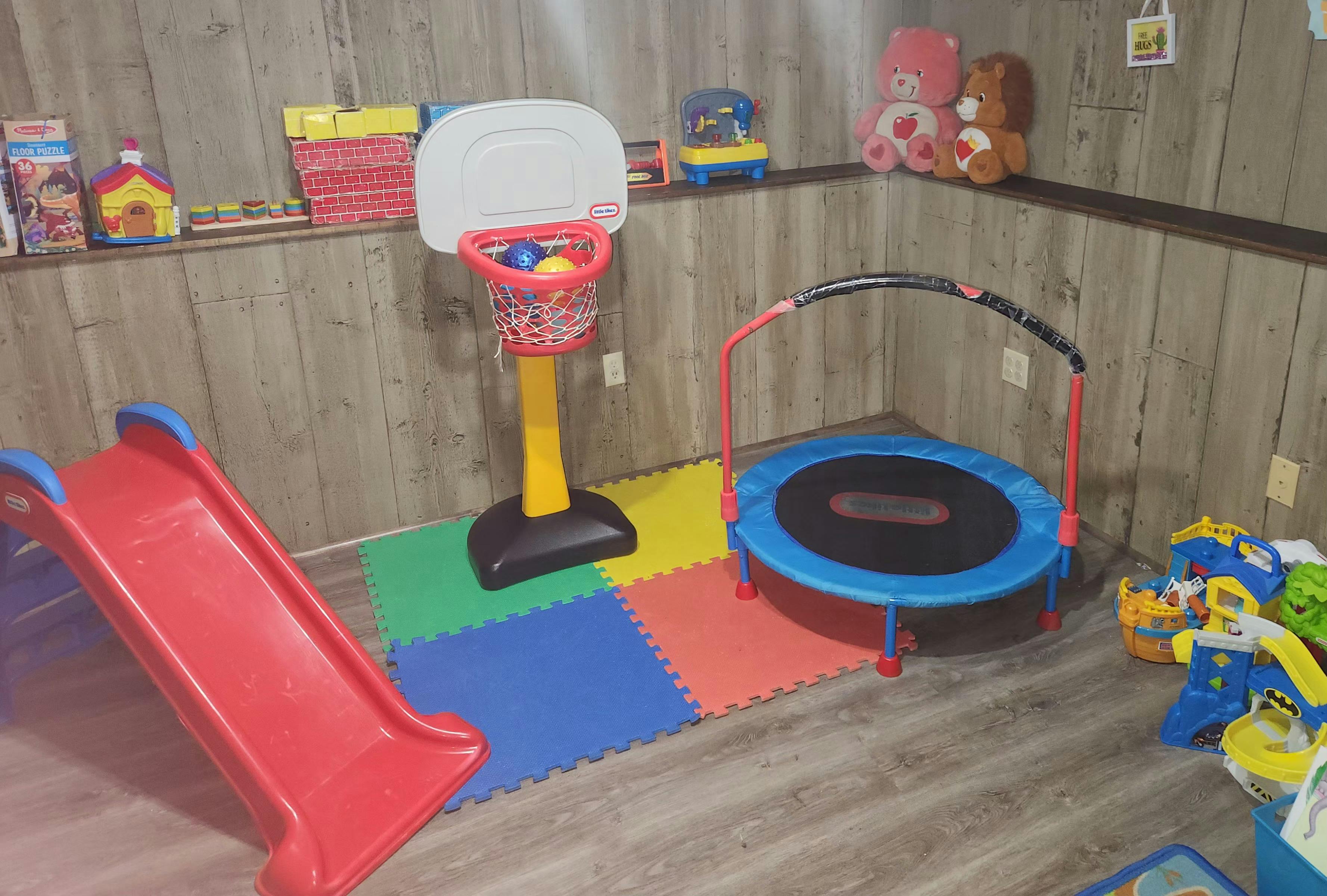 Child's play area with a slide, basketball hoop, and trampoline on colorful mats