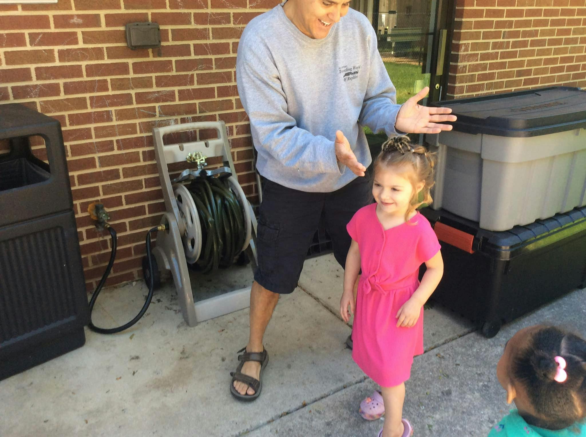 Person with hands out talking to a child in a pink dress