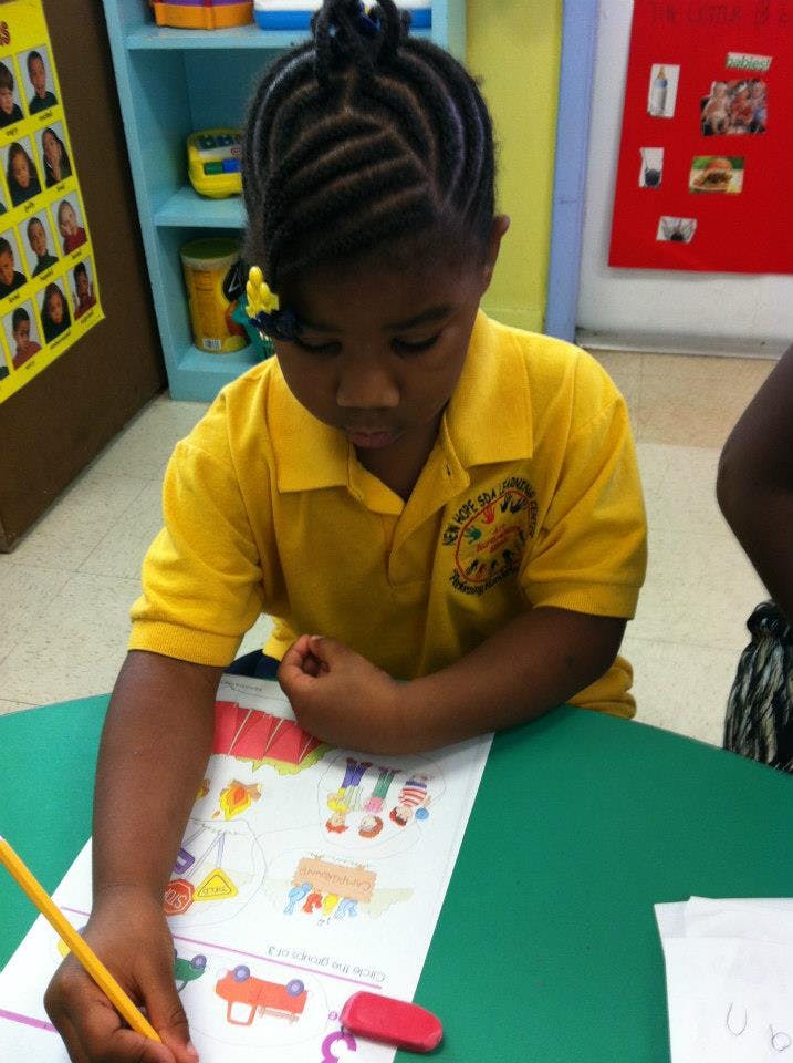 Child drawing on paper with a pencil in a classroom