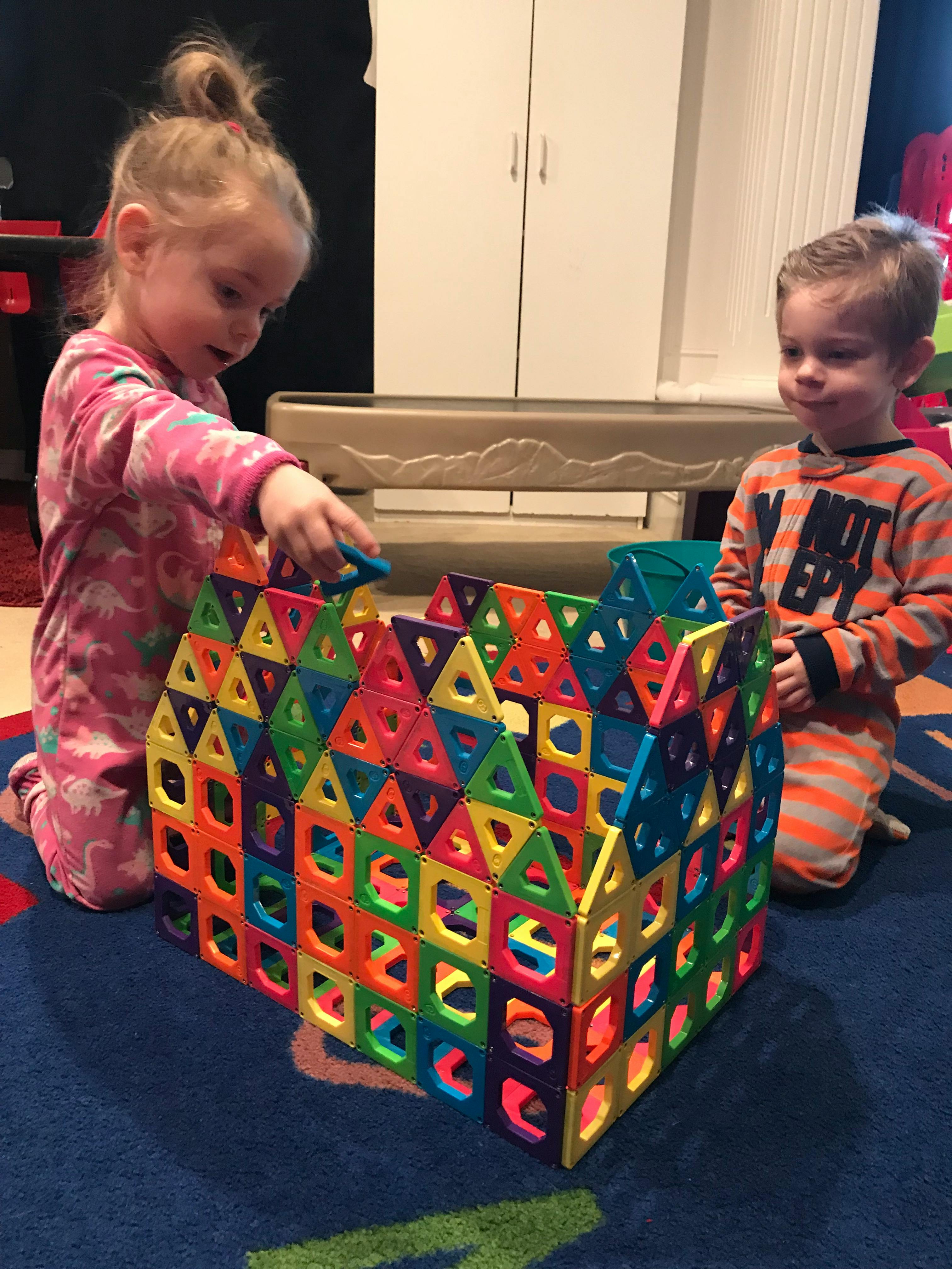 Two children playing with colorful magnetic tiles on the floor