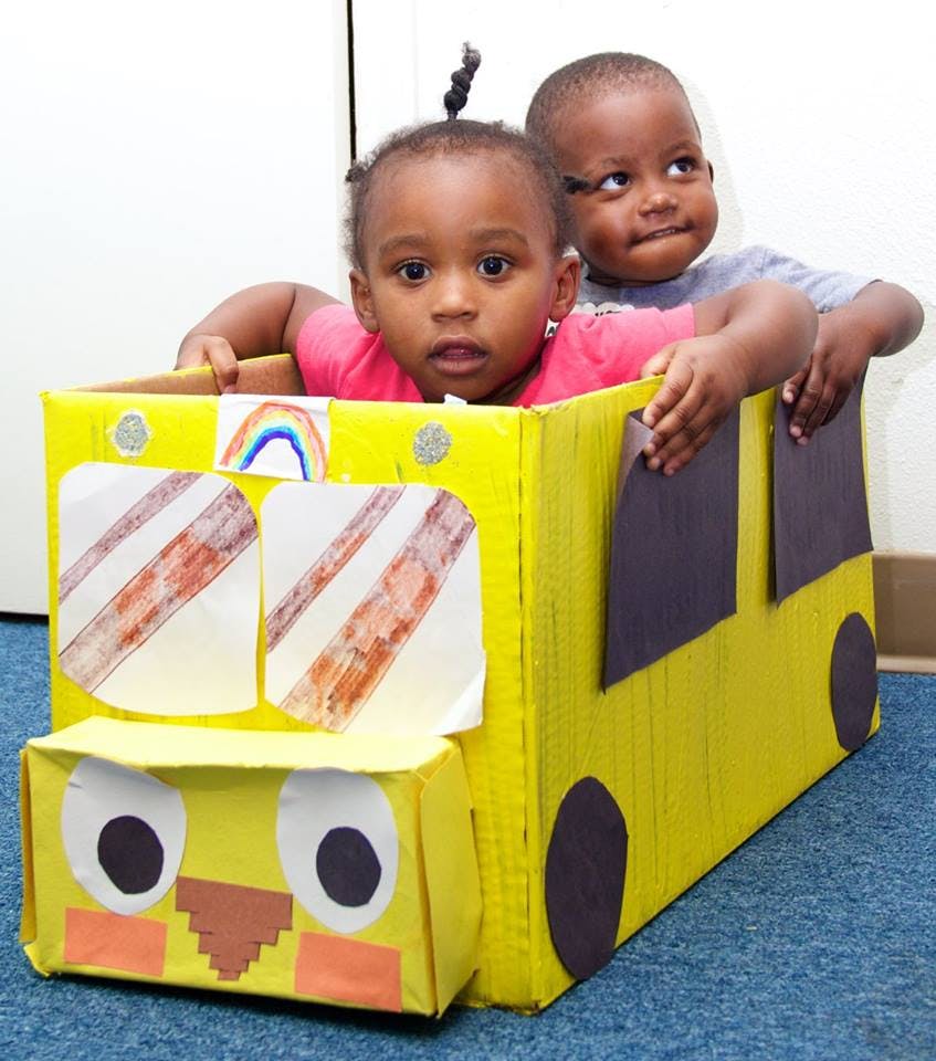 Two children in a yellow cardboard box bus