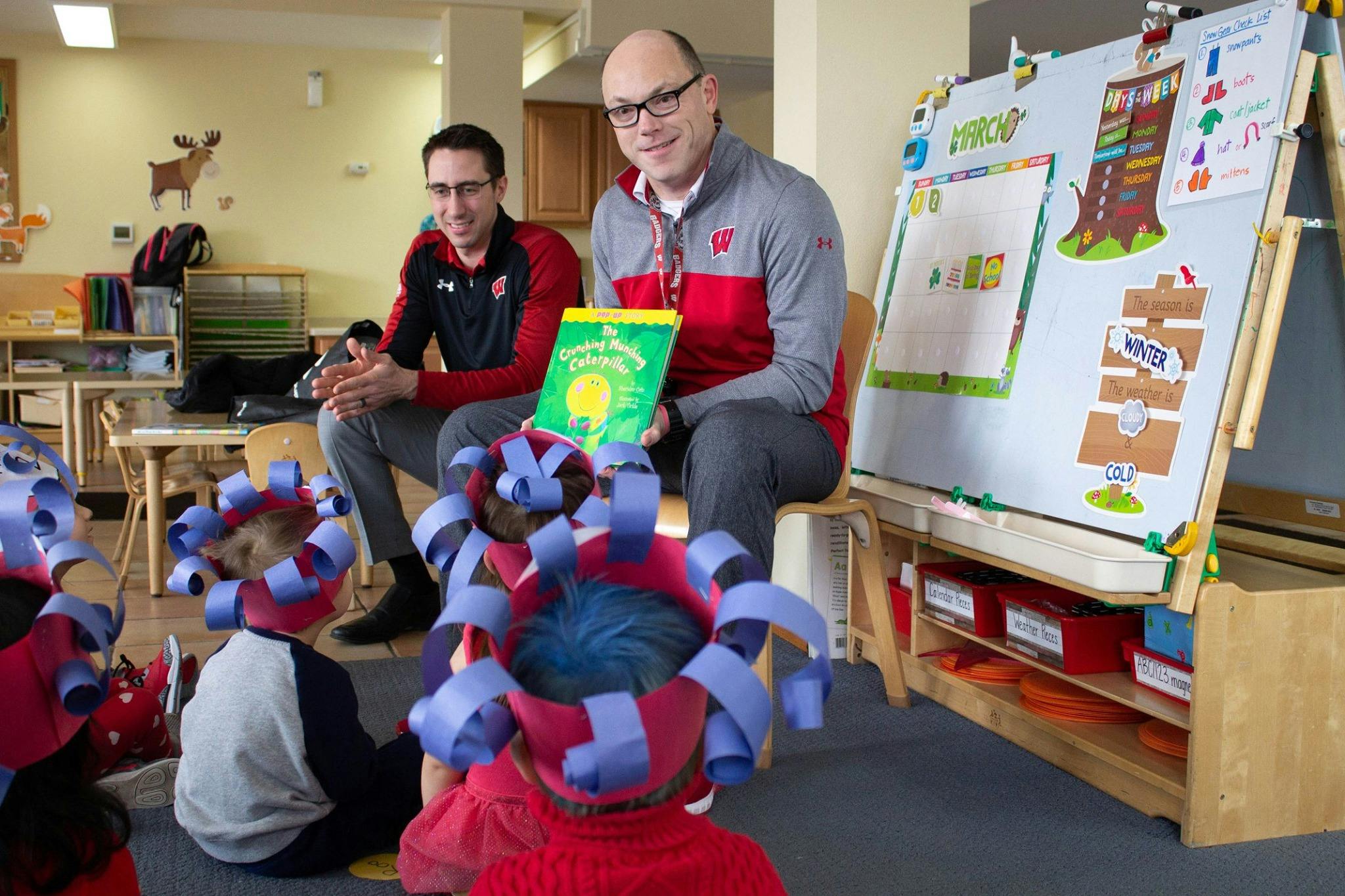 Two people reading a book to children in a classroom