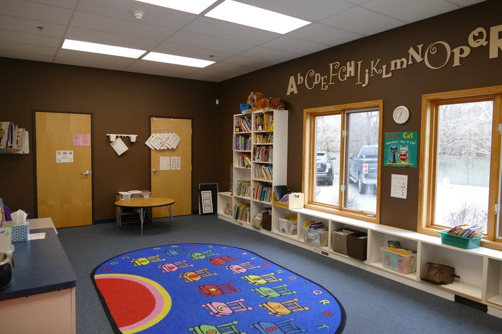 Classroom with alphabet on wall, windows, bookshelves, and a colorful rug