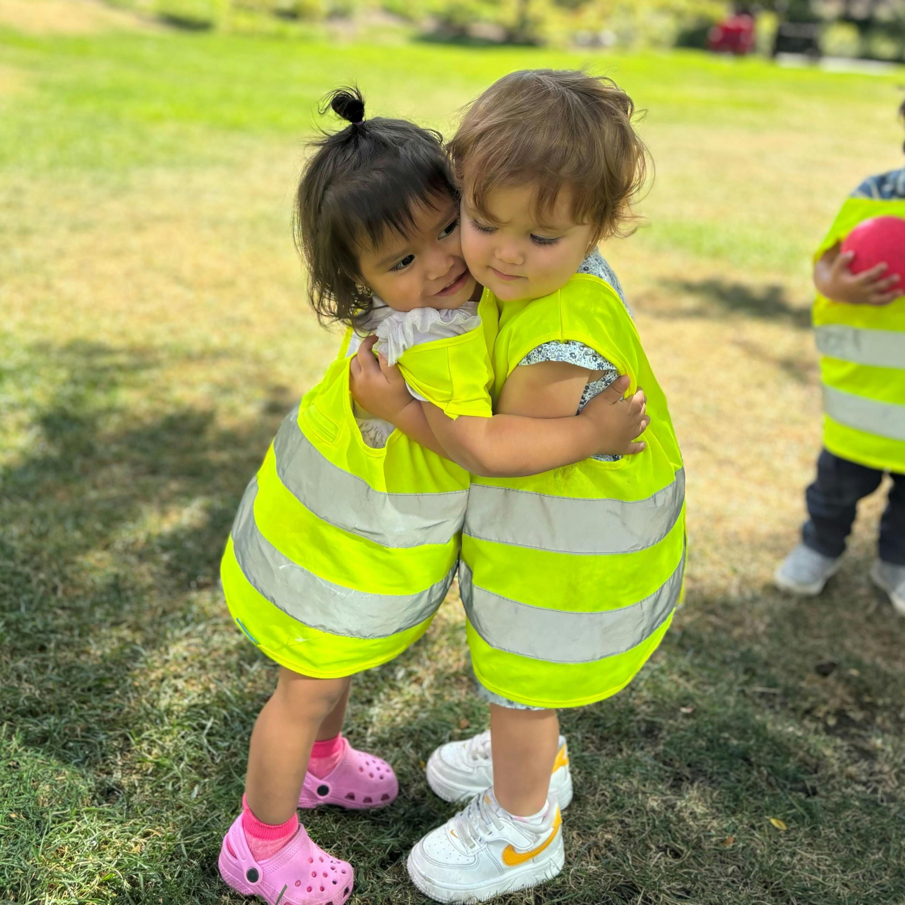 Two children in safety vests hugging outdoors