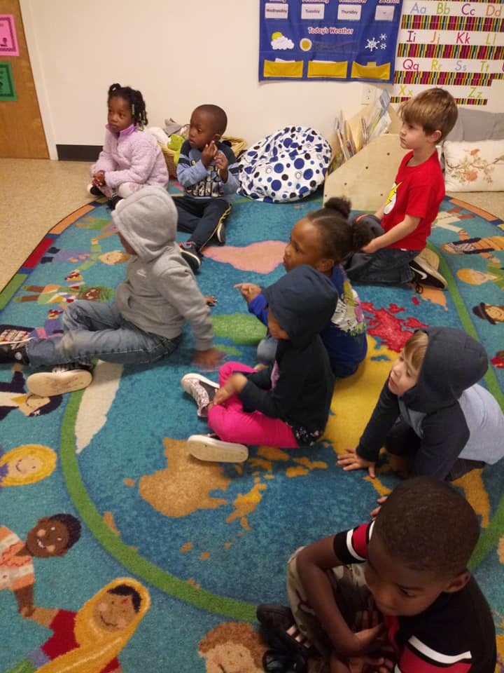 Group of children sitting on a colorful rug in a classroom