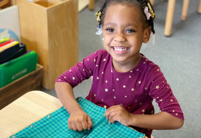 Child with braided hair and purple shirt holding a green checkered book