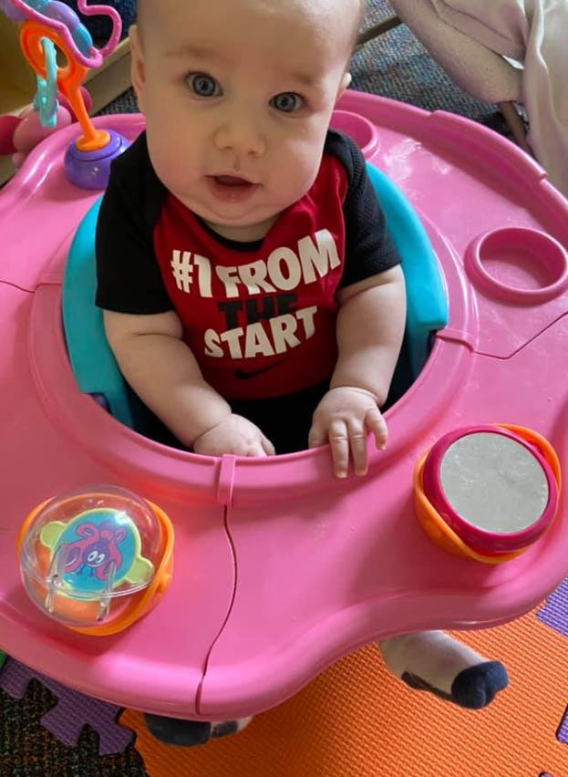 Child in a pink activity center wearing a red shirt with "#1 FROM THE START"