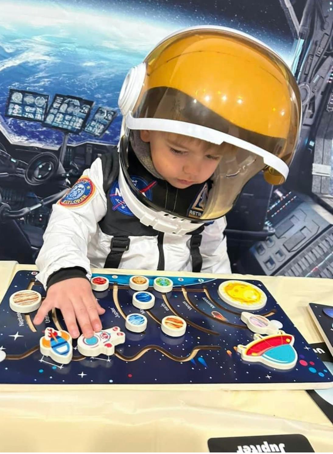 Child in astronaut helmet and suit playing with a space-themed board game