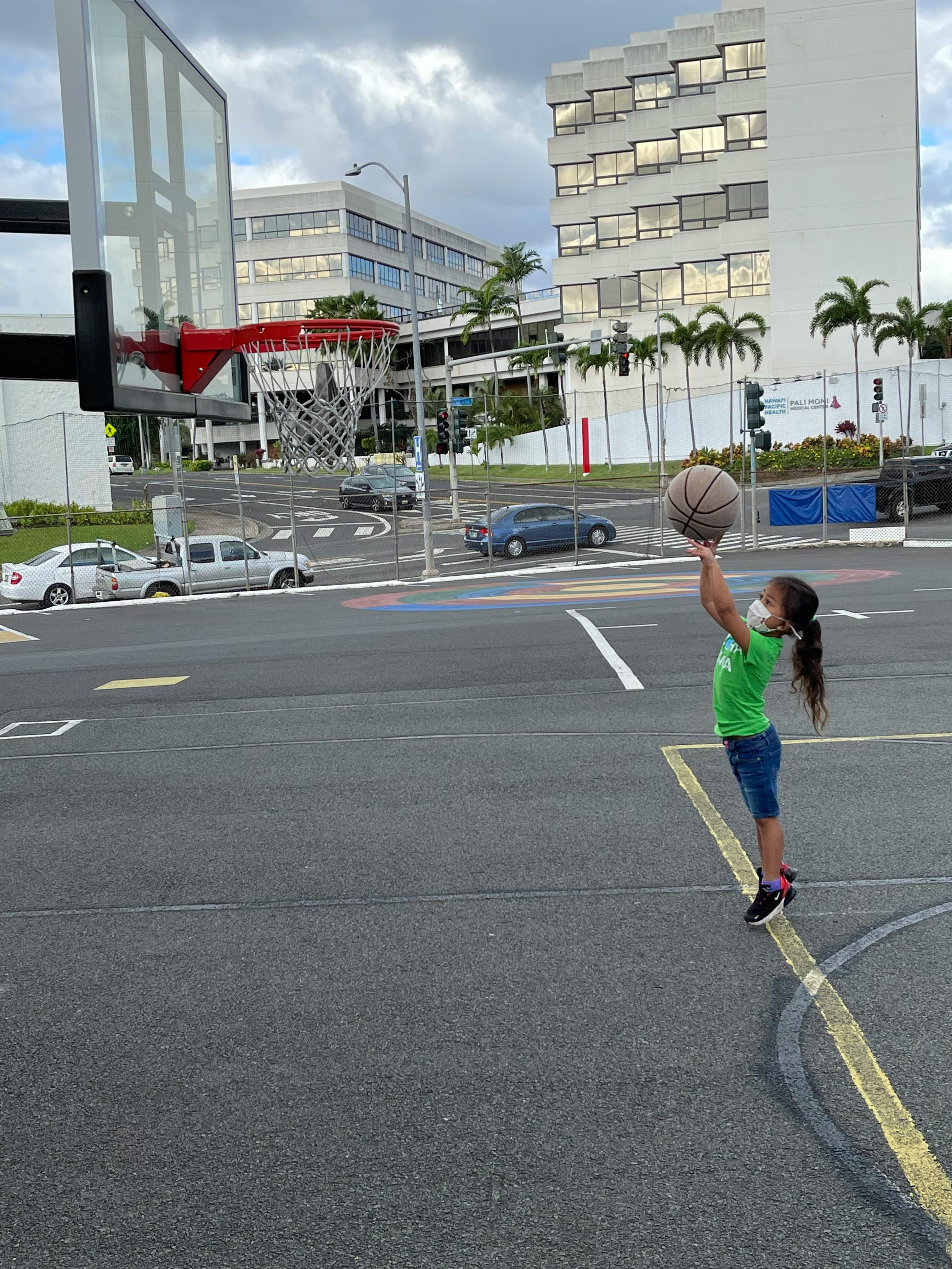 Child in a mask shooting a basketball toward a hoop