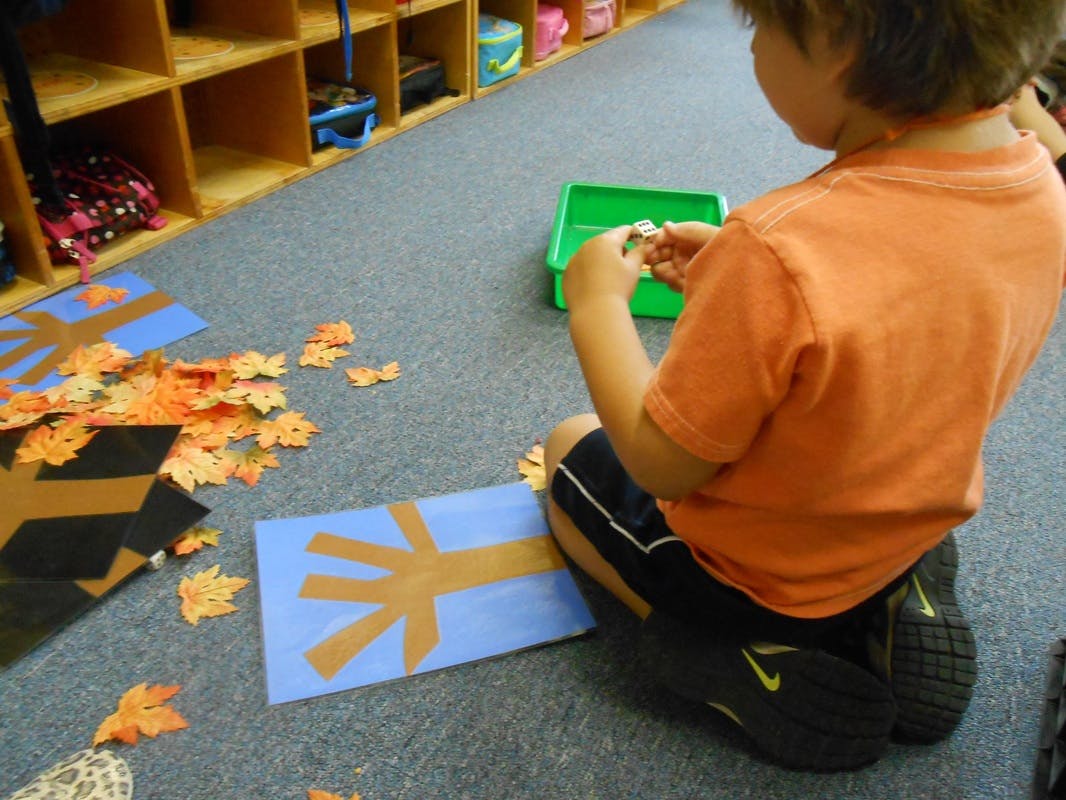 Child sitting on floor making a craft with paper leaves