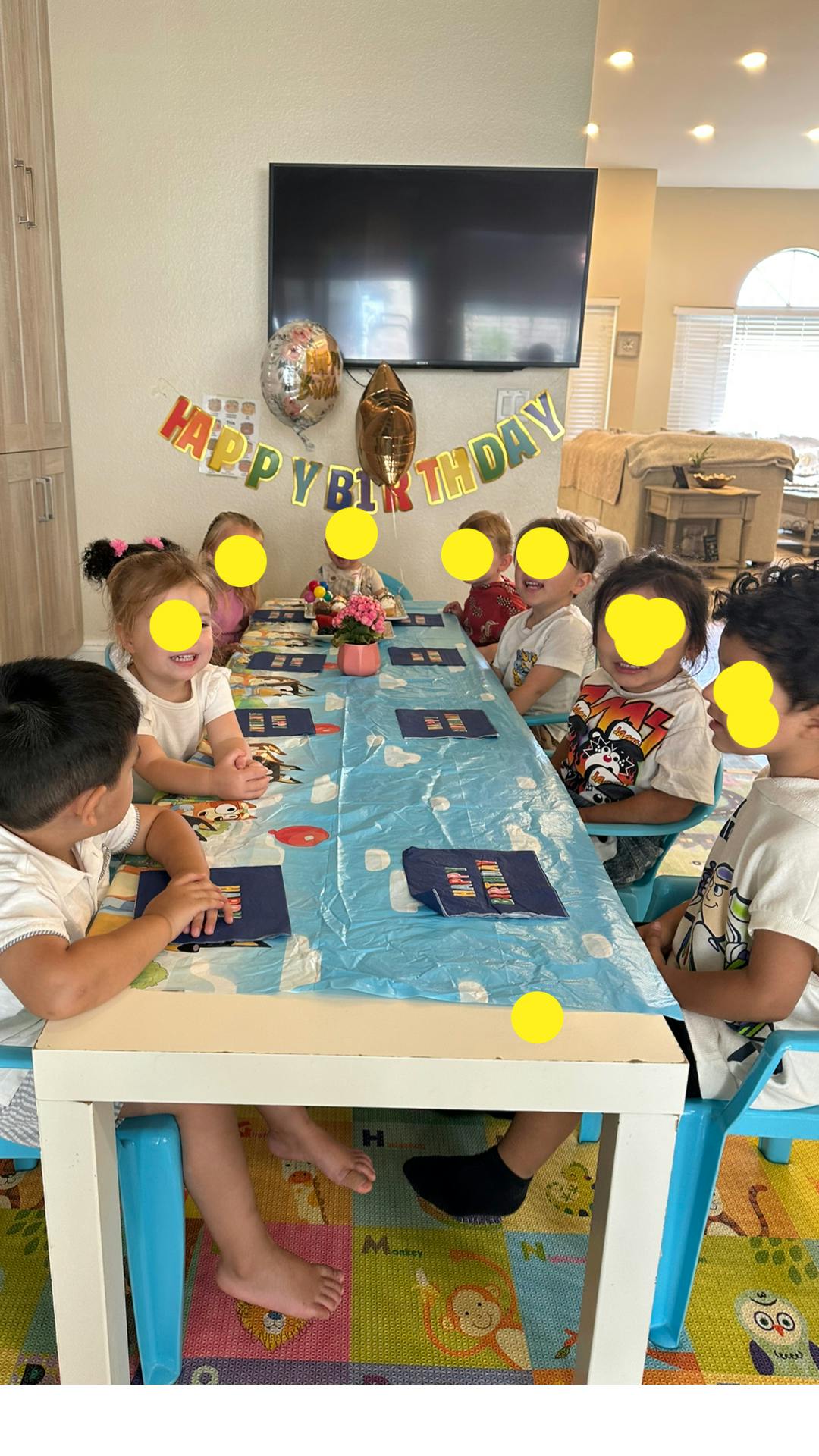 Group of children seated at a table with a "Happy Birthday" banner and balloons