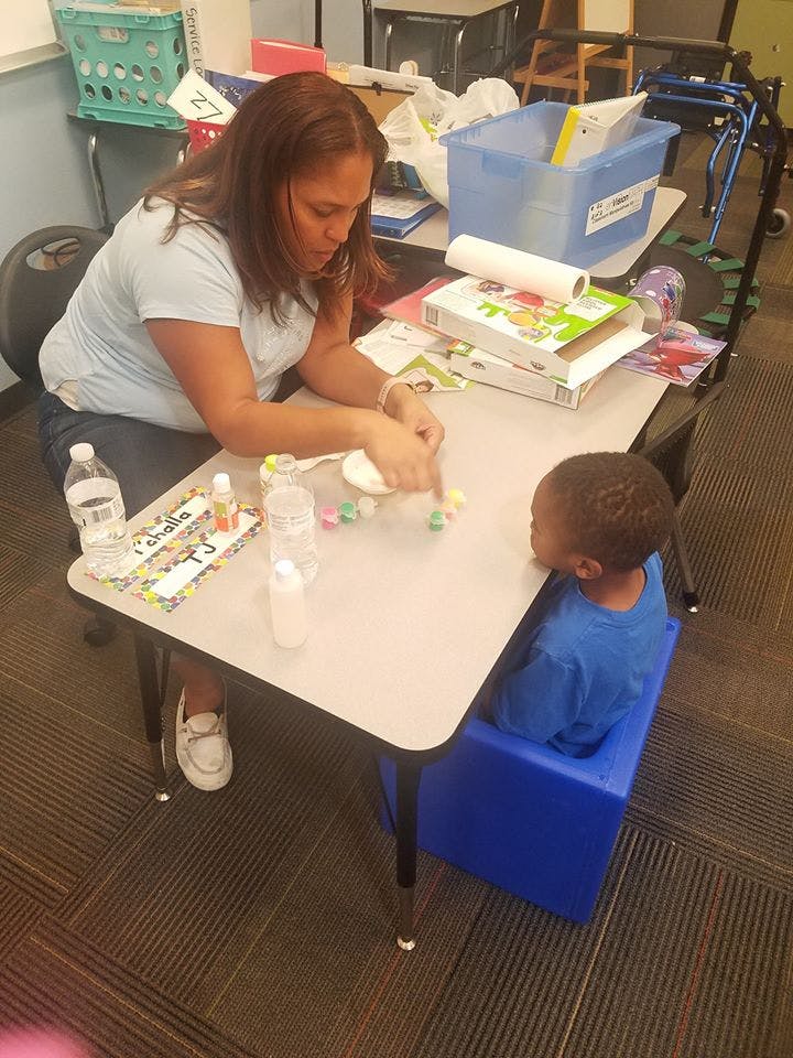 Person and child at a table doing an activity with small objects