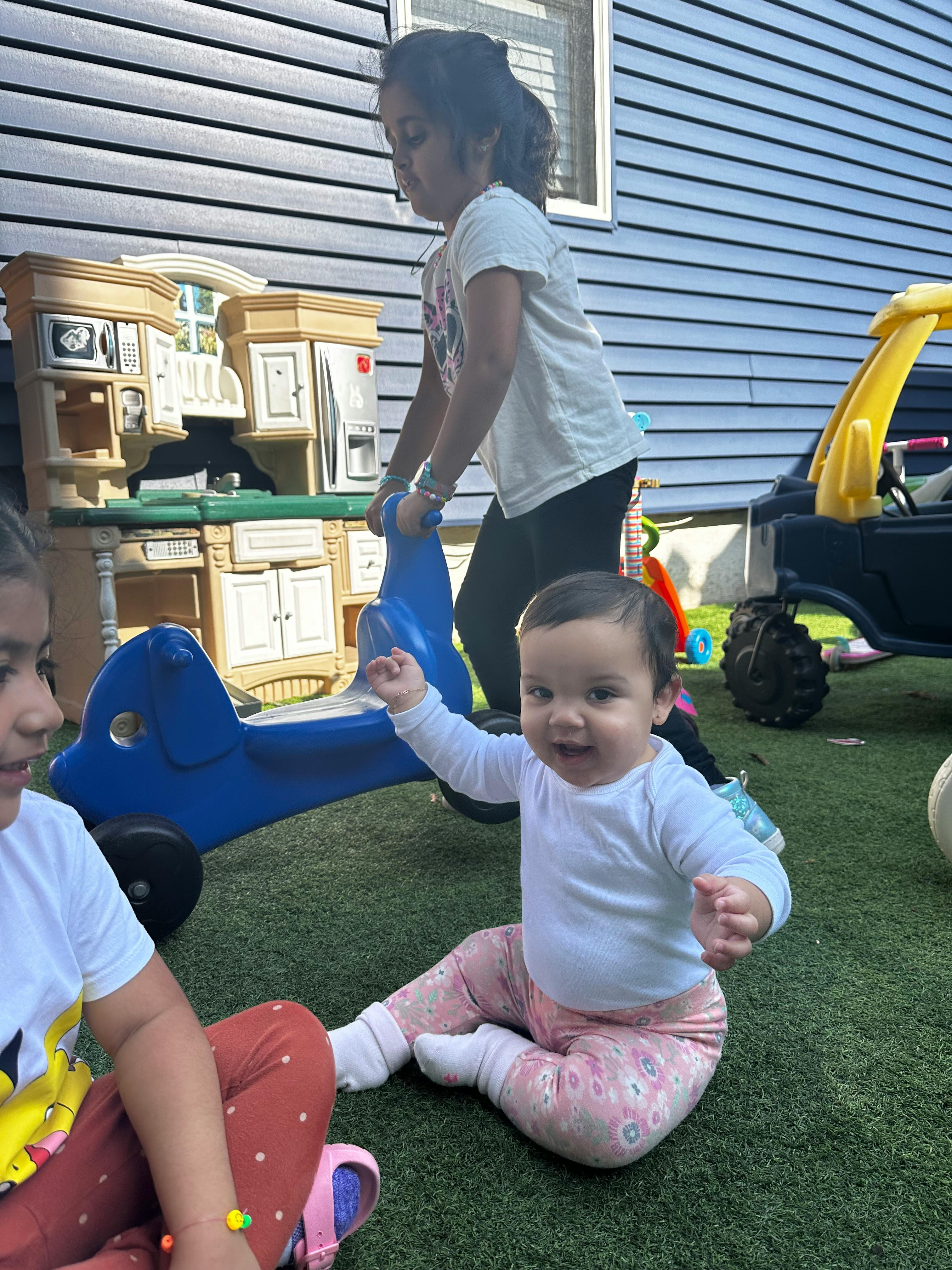 Child pushing a blue toy, baby sitting on grass