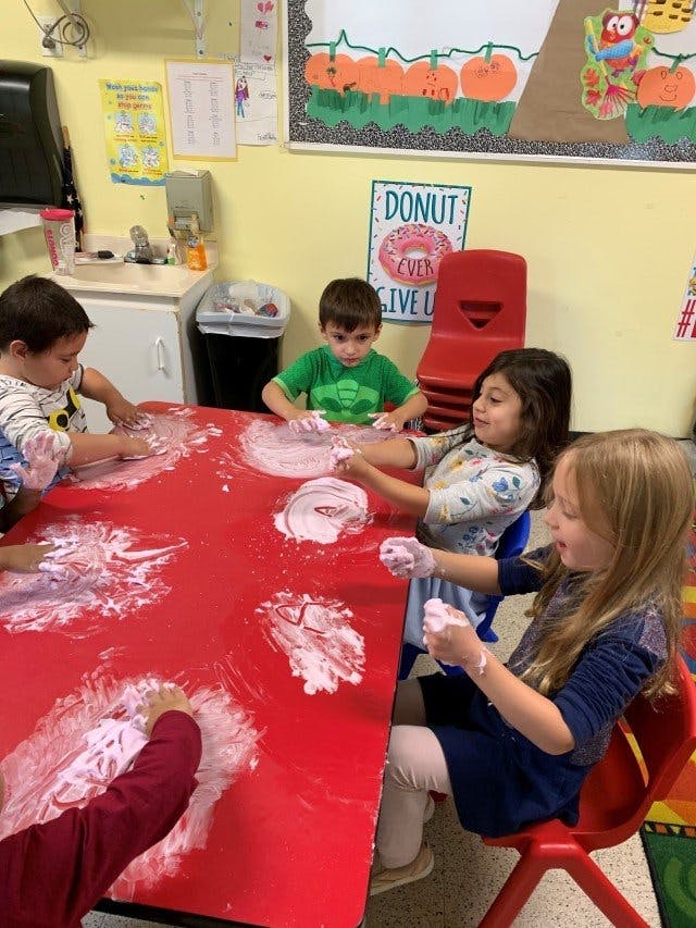 Children playing with shaving cream on a red table