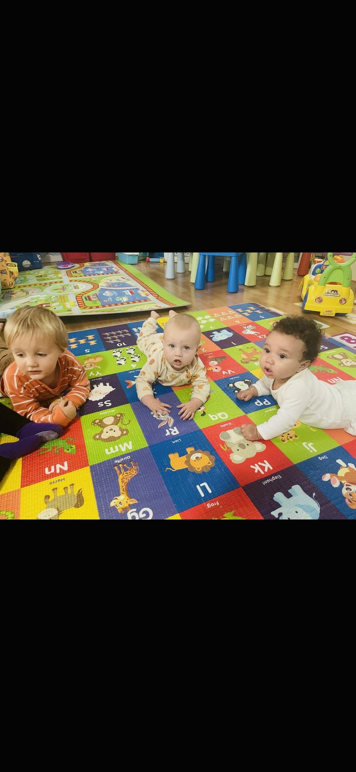 Three children crawling on a colorful alphabet playmat in a room