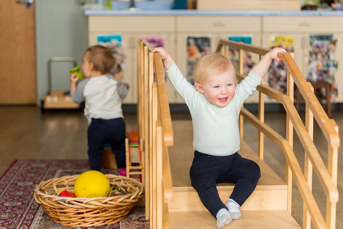 Child sitting on a small wooden slide with arms raised
