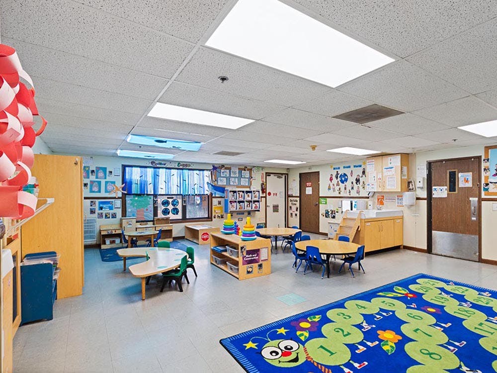 Empty classroom with small tables and chairs, colorful rug
