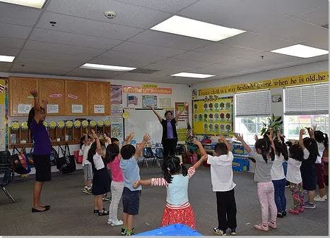 Adults and children with arms raised in a classroom