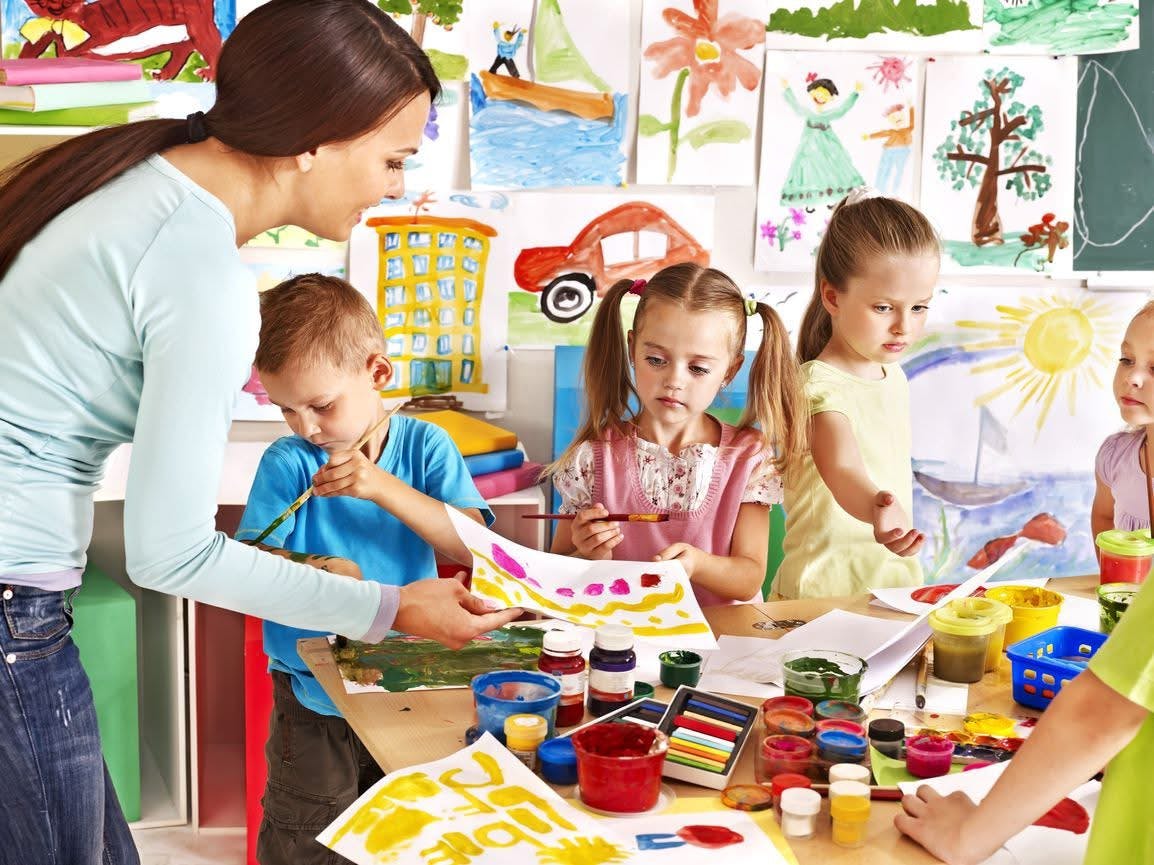 Adult assisting children with painting in a classroom
