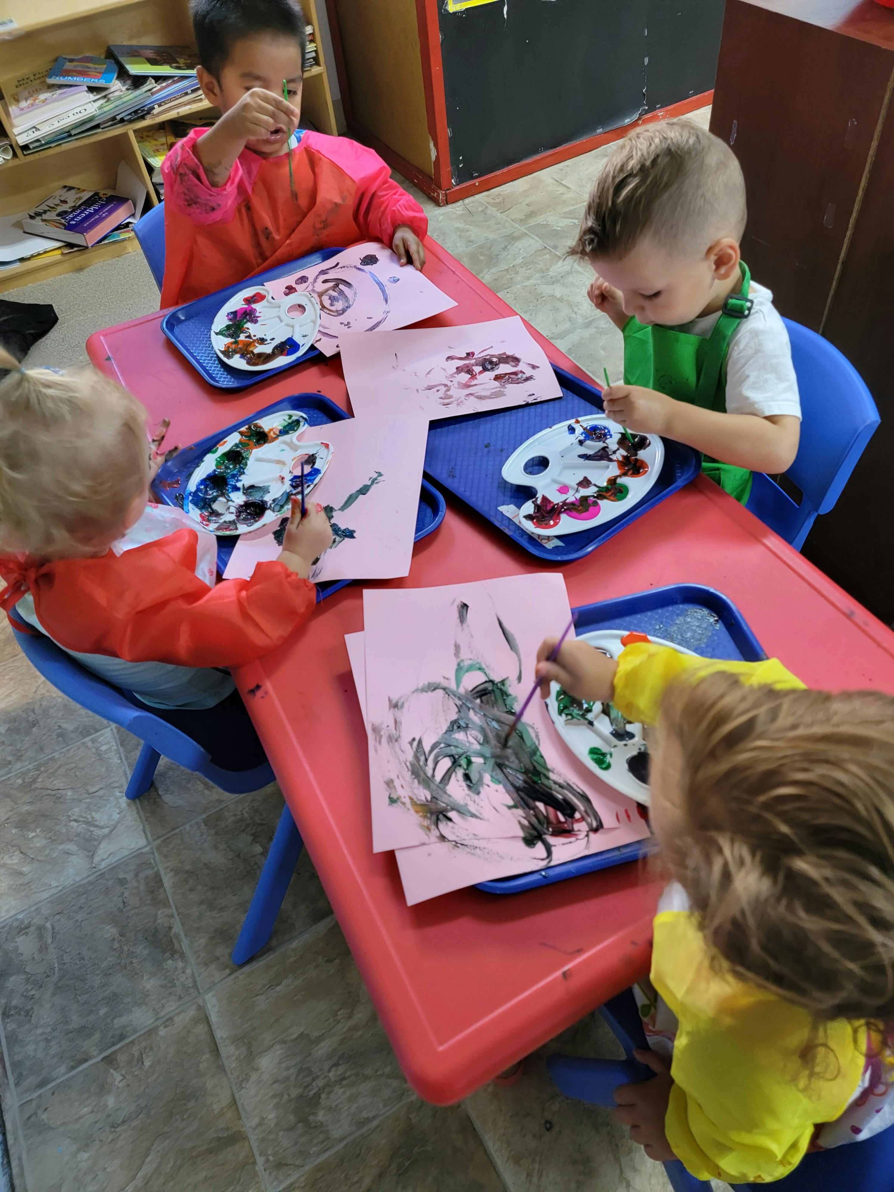 Four children painting at a red table