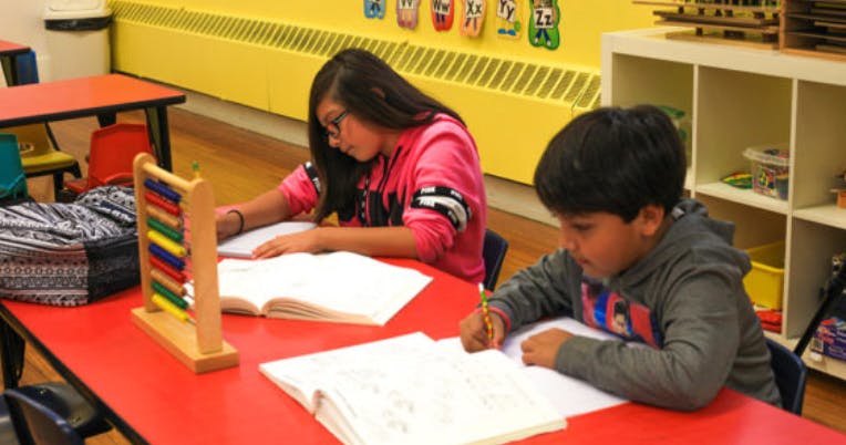 Two children writing at a table in a classroom