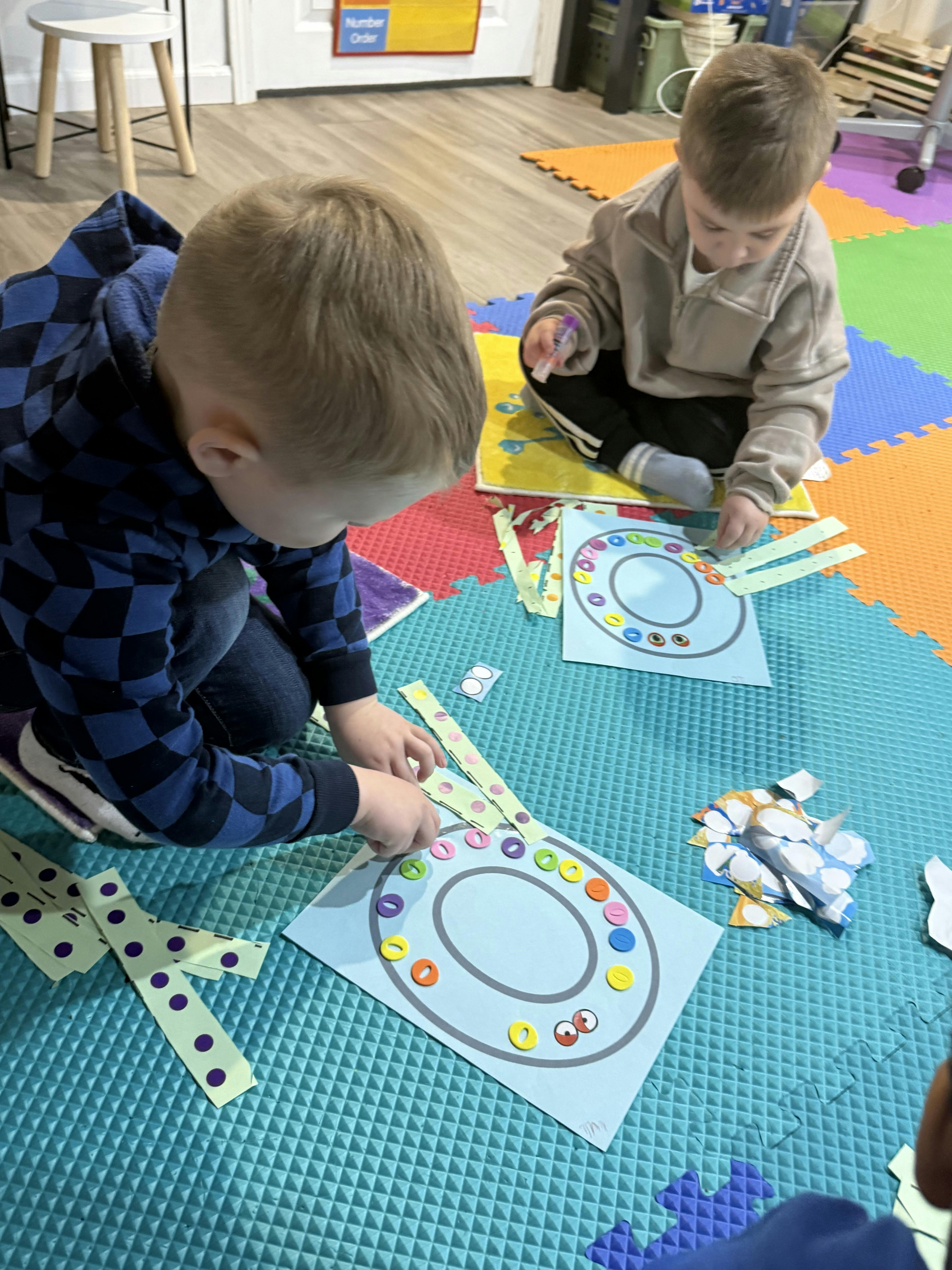Two children on floor mats, one placing colorful circles on a paper