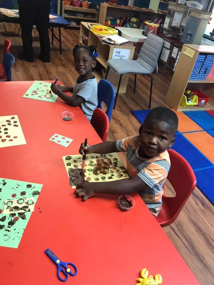 Two children painting at a red table in a classroom
