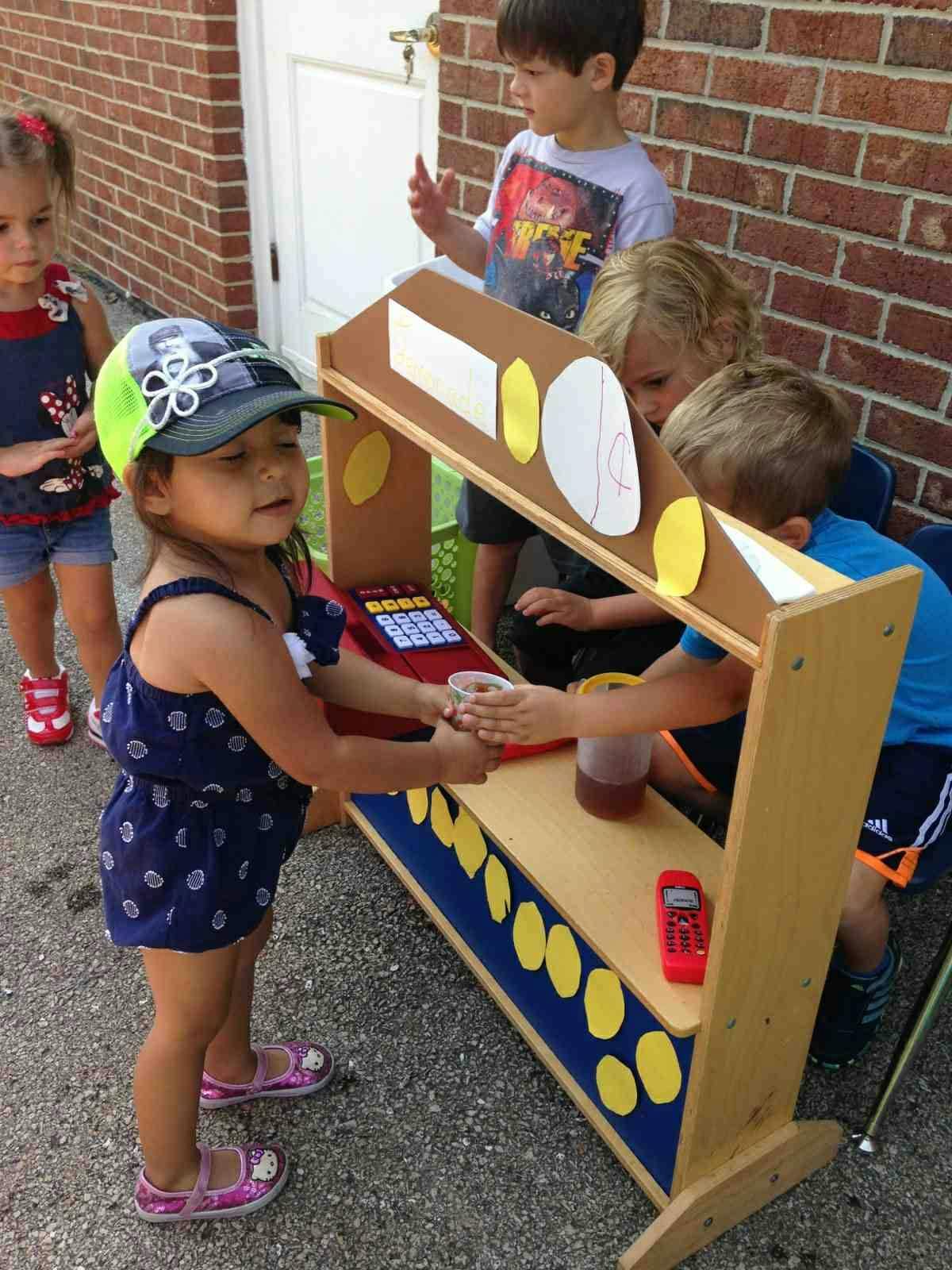Child in a hat serving a drink from a play stand to another child