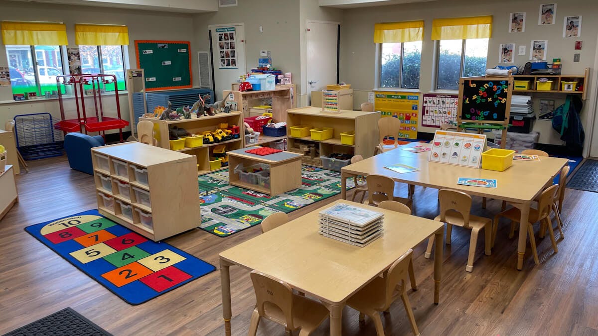 A colorful classroom with play mats, small tables, and shelves of toys
