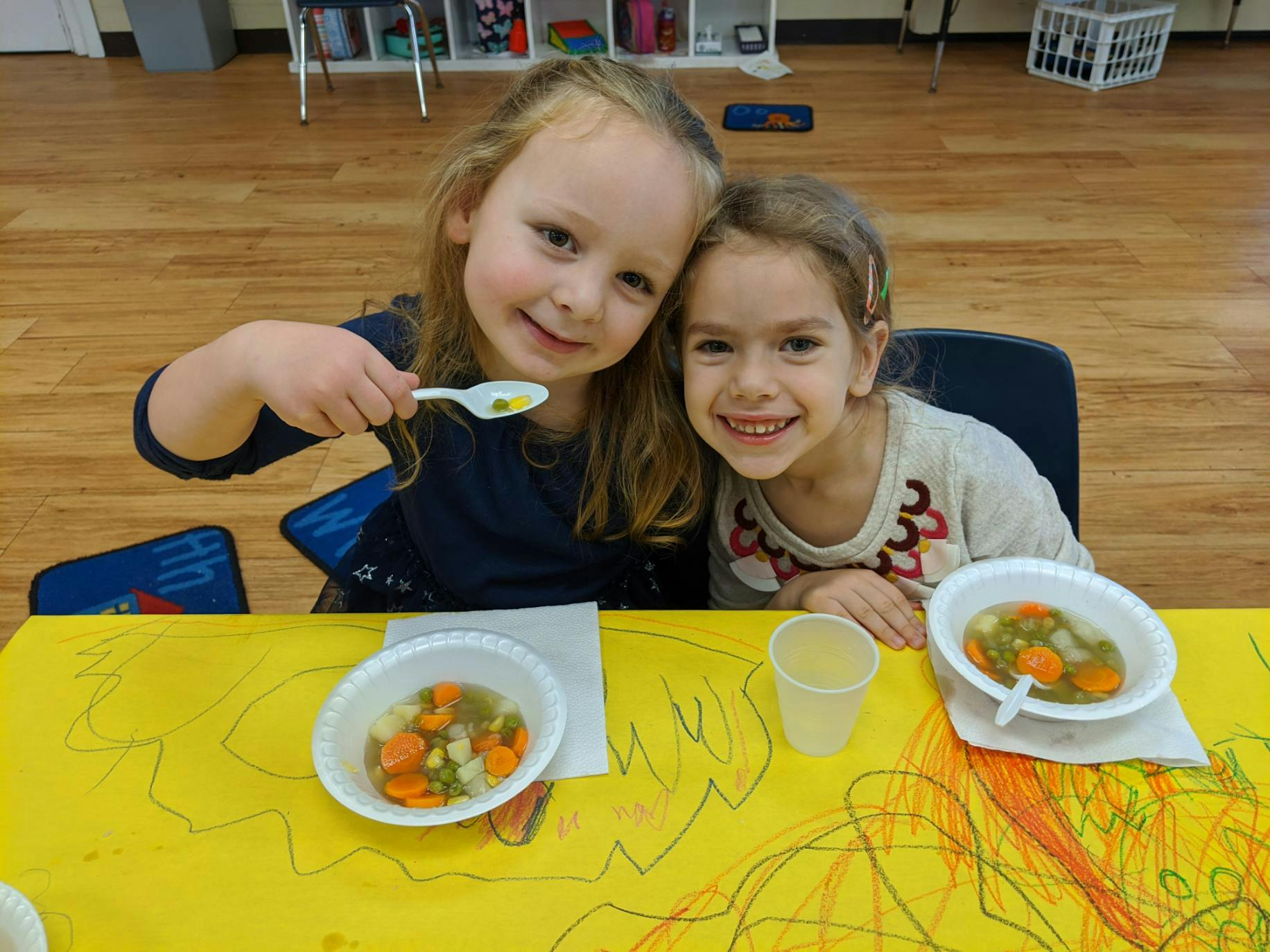 Two children sitting at a table with bowls of soup