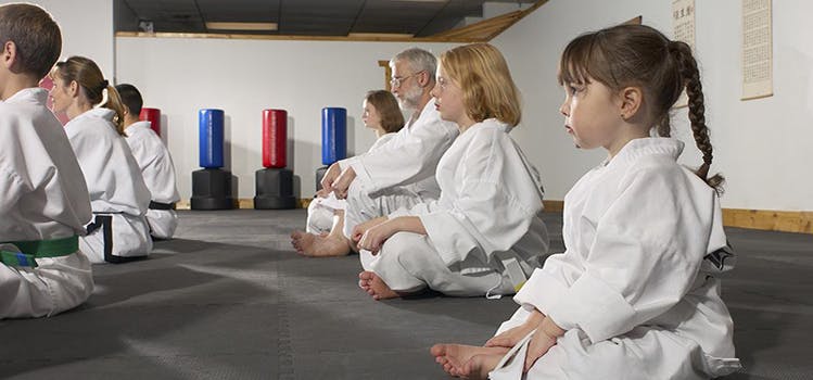 People in white martial arts uniforms sitting on a mat