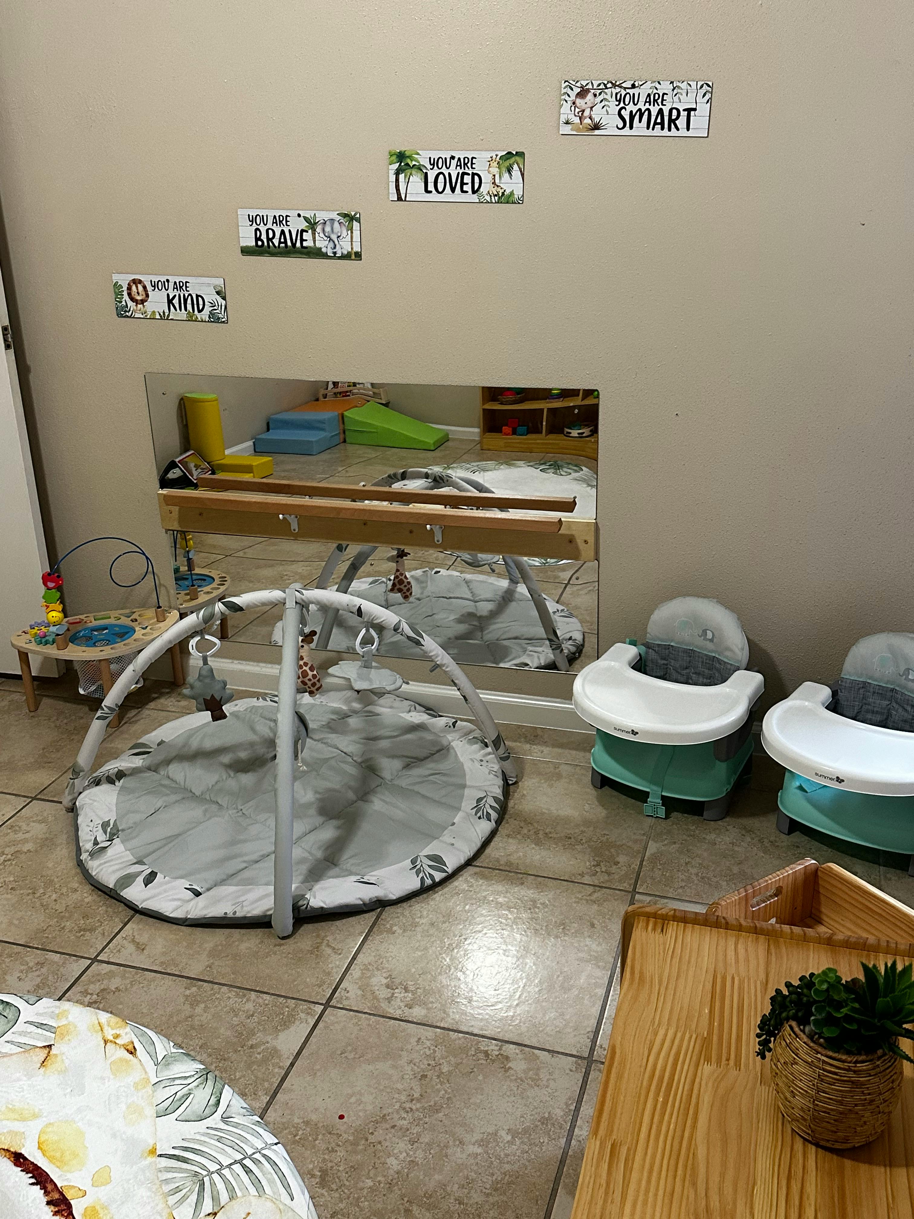 Infant play area with a play mat, baby seats, and wall decor
