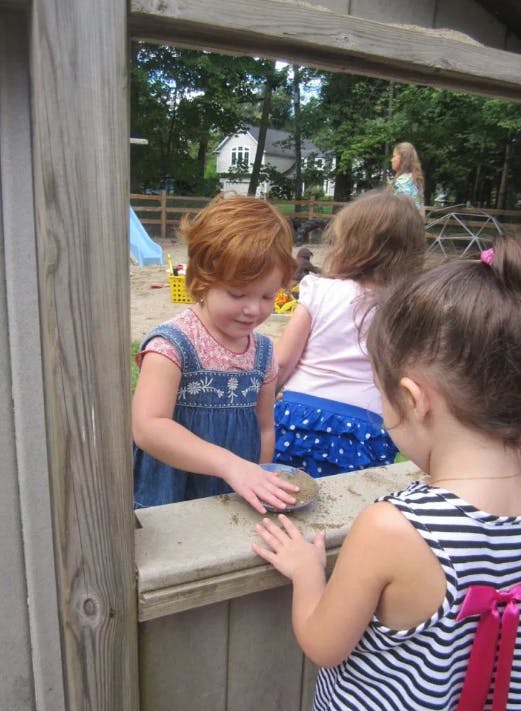 Child in denim dress playing with sand at a counter with other children