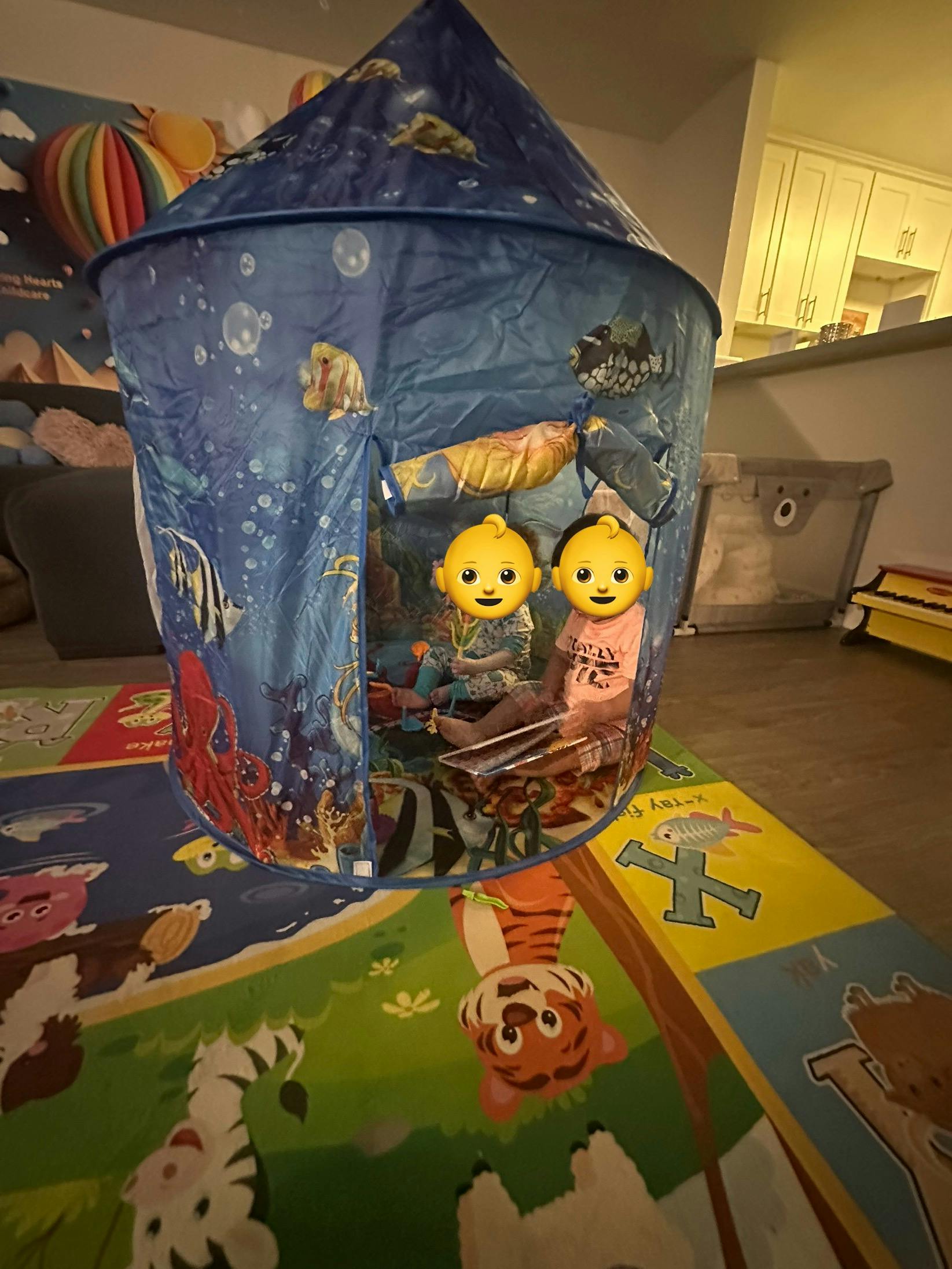 Two children sitting inside a blue play tent decorated with an underwater scene