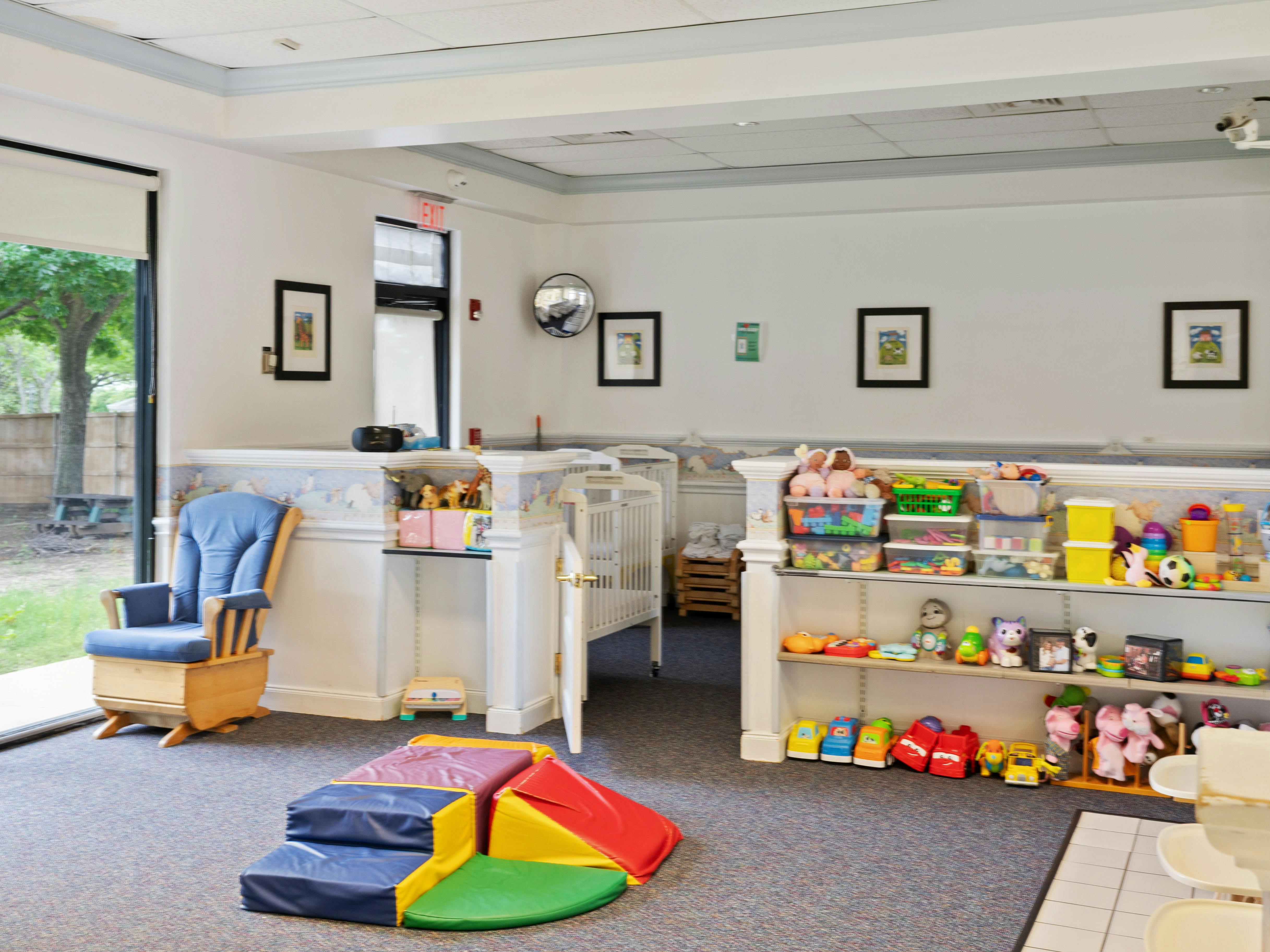 Baby room with cribs, rocker, play mat, and shelves of toys