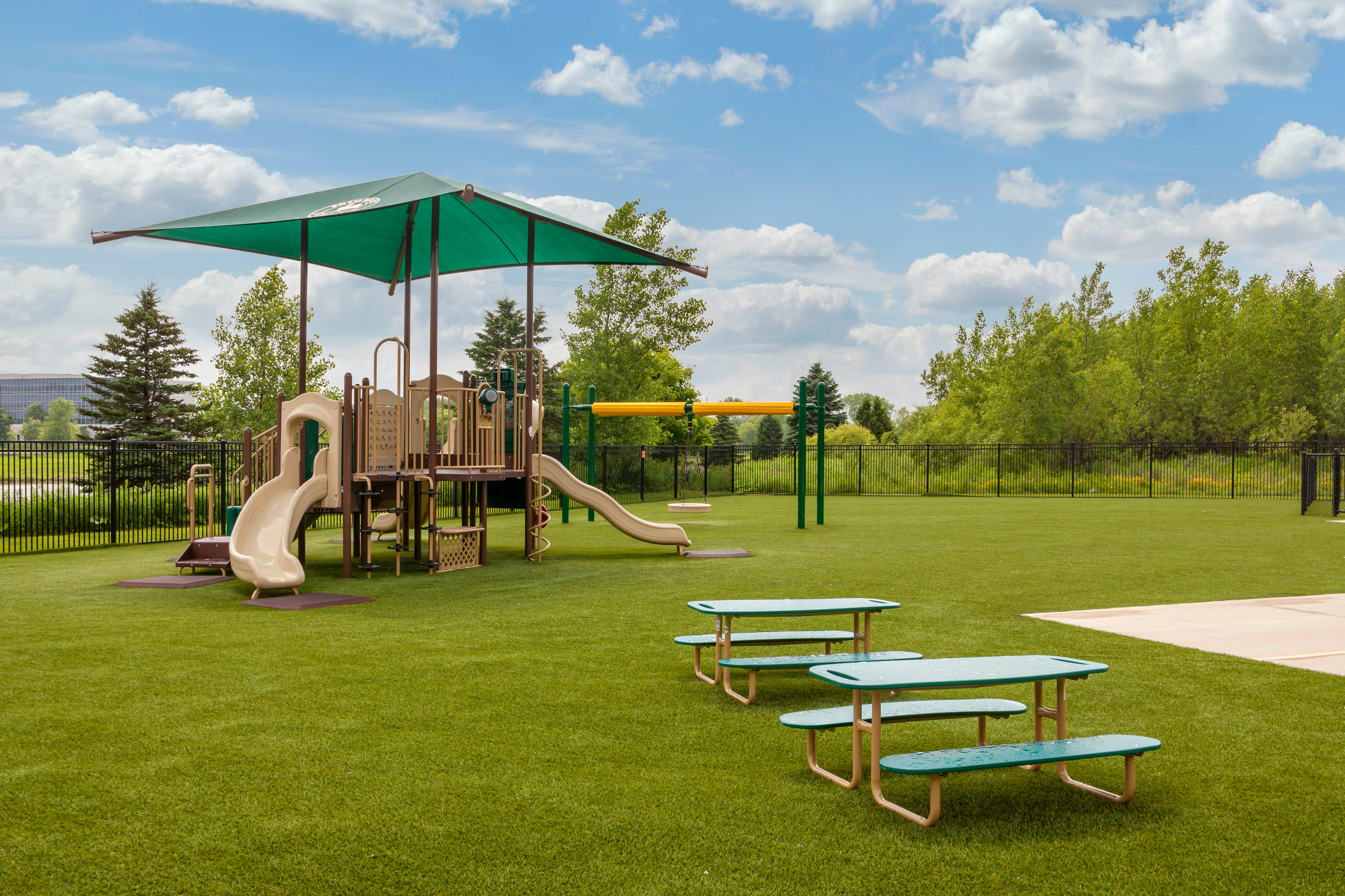 Empty outdoor playground with slides, swings, and picnic tables on artificial turf