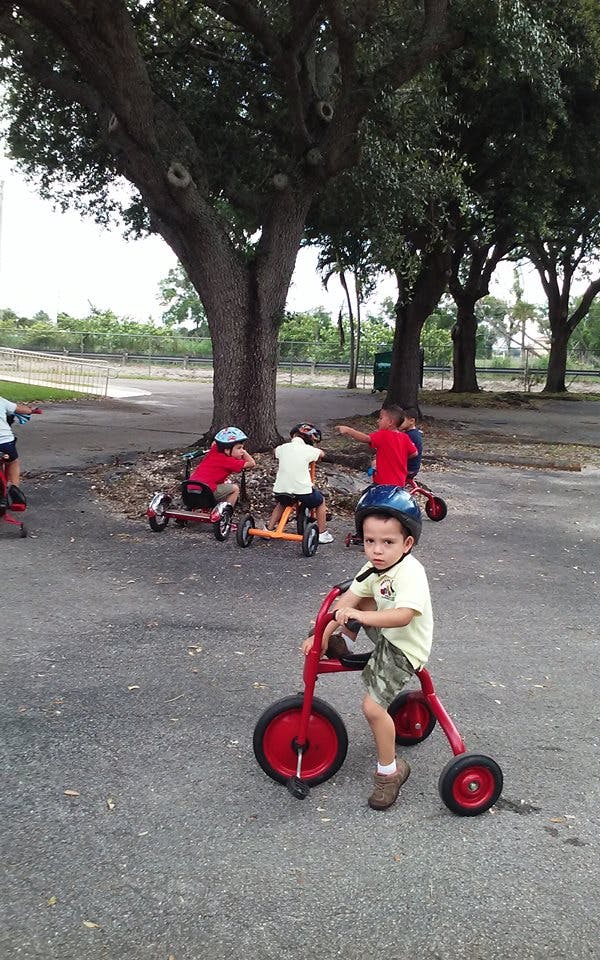 Child in helmet on red tricycle with other children on tricycles in background
