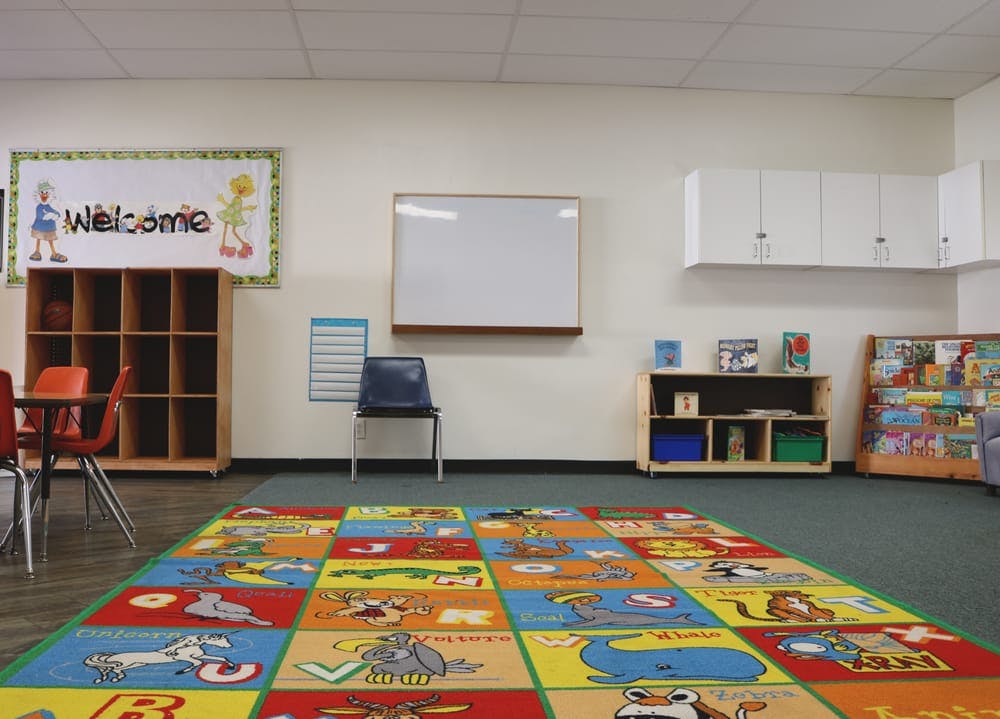 Empty classroom with a colorful alphabet rug, whiteboard, and cubbies