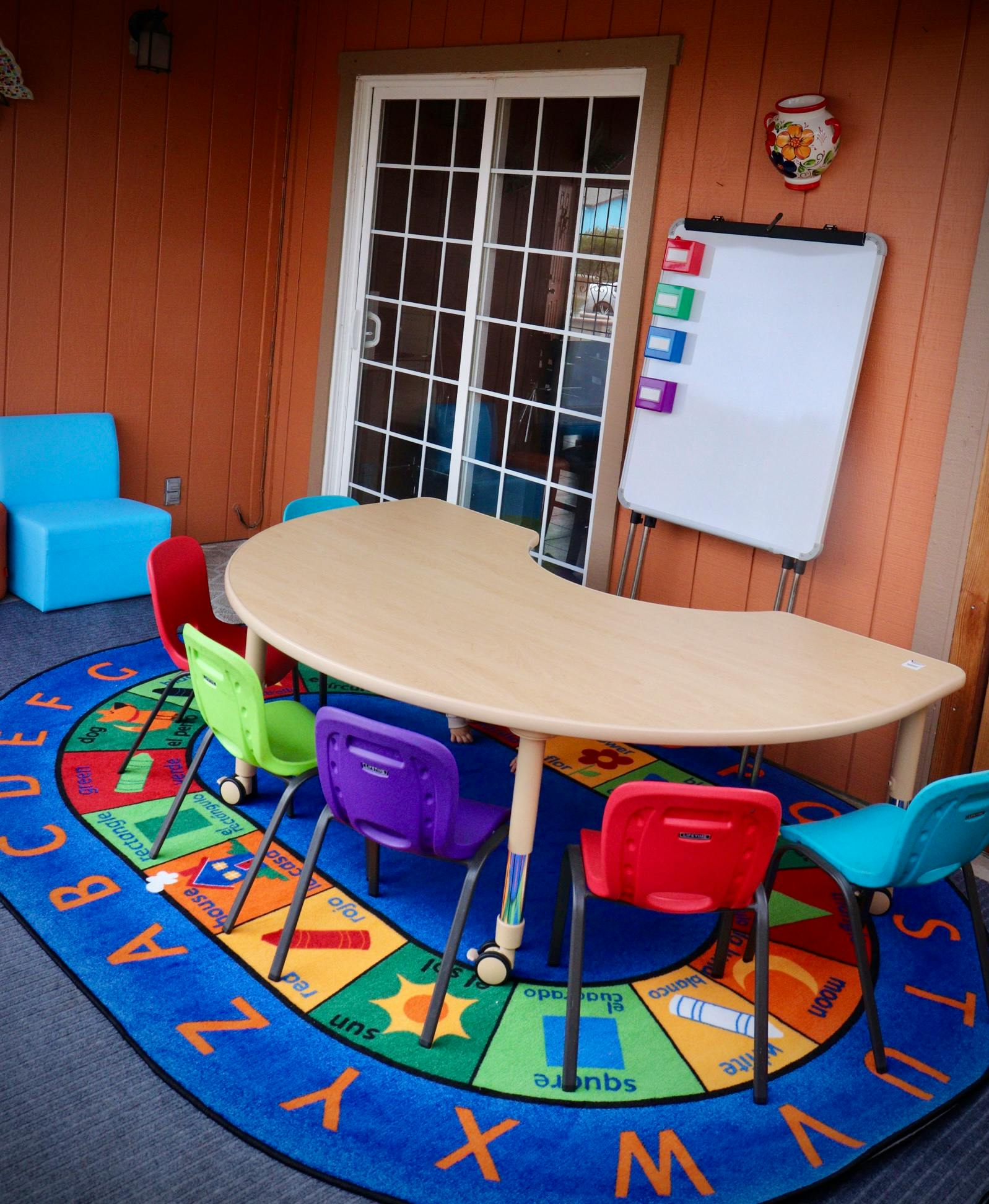 Classroom with a curved table, colorful chairs, and an alphabet rug